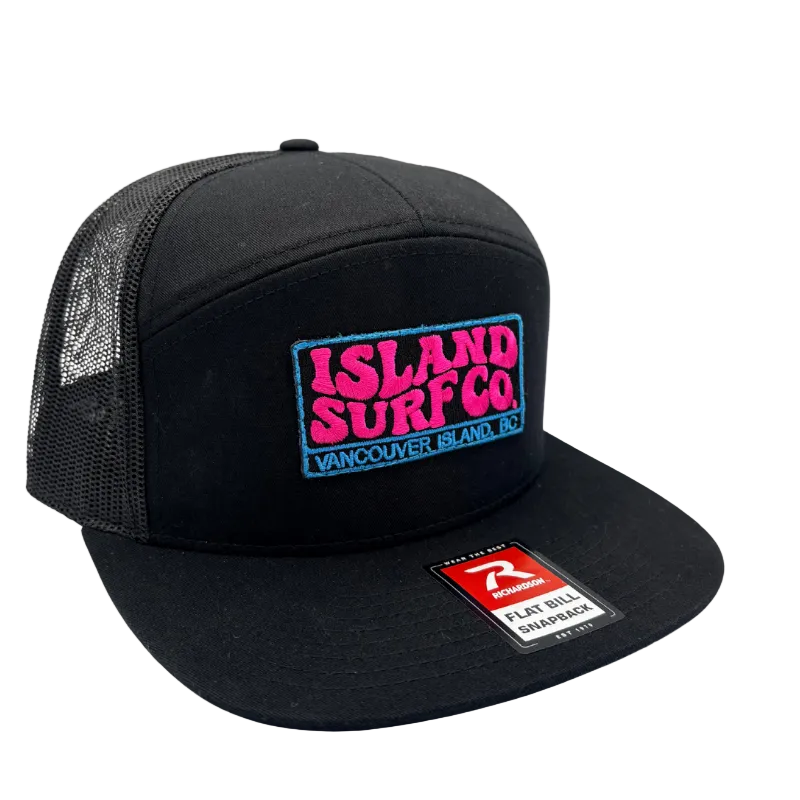 A black trucker-style snapback cap with a mesh back, featuring a colorful embroidered 'ISLAND SURF CO' patch on the front and a red and white Rip Curl flat bill sharpener sticker on the brim.