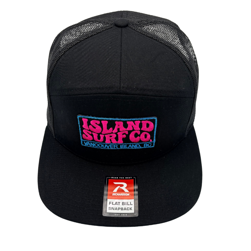A black trucker hat with a curved brim, featuring a front patch that reads 'ISLAND SURF CO. VANCOUVER, ISLAND, BC' in pink and blue, and a visible flat bill snapback sticker from Rawlings.